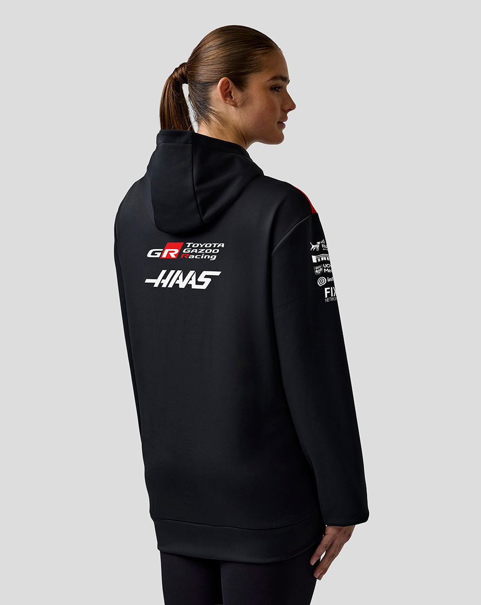 Person wearing a black hoodie with racing team logos on a gray background