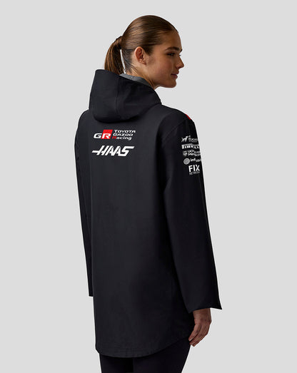 Person wearing a black jacket with various logos on the back against a light gray background