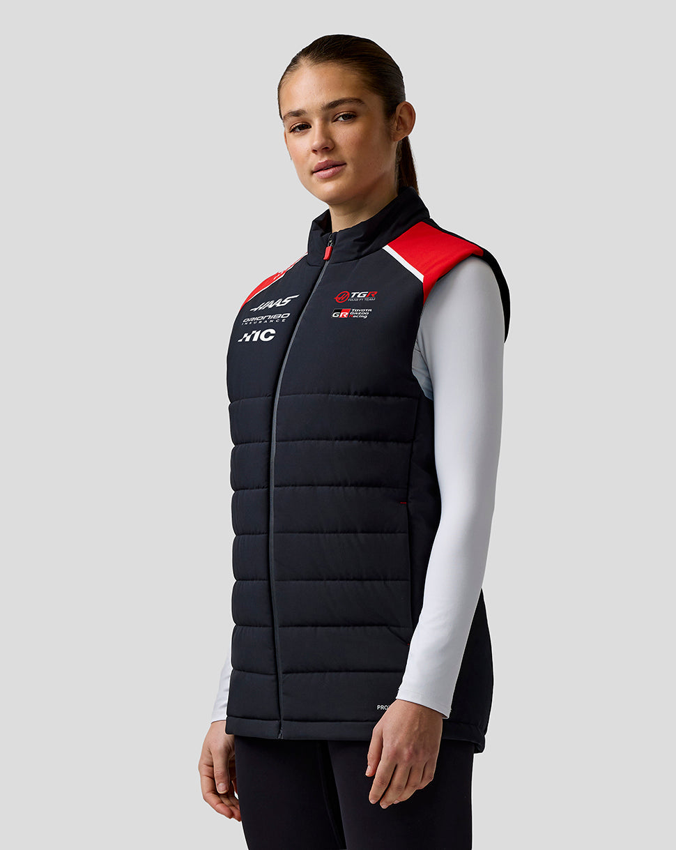 Person wearing a black puffer vest with red and white accents on a gray background